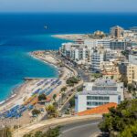 Superbe vue aérienne du paysage urbain et du littoral de Rhodes, mettant en valeur les plages animées et les eaux azur.