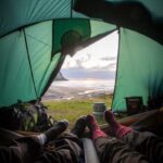 Vue de l'intérieur d'une tente surplombant un coucher de soleil côtier, capturant une expérience de camping relaxante.