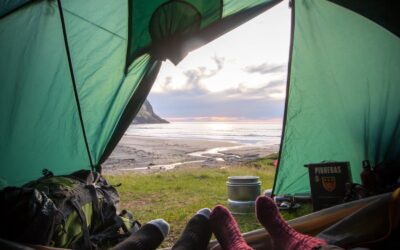 Vue de l'intérieur d'une tente surplombant un coucher de soleil côtier, capturant une expérience de camping relaxante.
