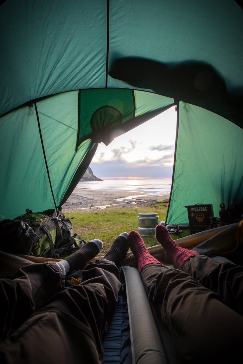 Vue de l'intérieur d'une tente surplombant un coucher de soleil côtier, capturant une expérience de camping relaxante.